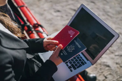 A person sitting on a bench using a laptop while holding two passports, illustrating the concept of digital identity, cybersecurity during travel, and secure handling of personal information online.