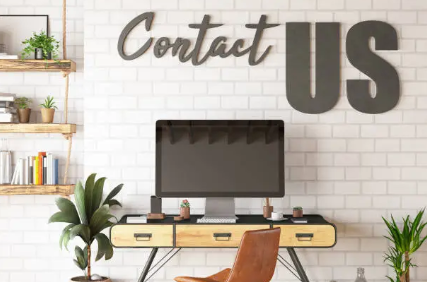 Contact Cyber Hackers Diary workspace with a desktop computer, indoor plants, and the words 'Contact Us' on a white brick wall.